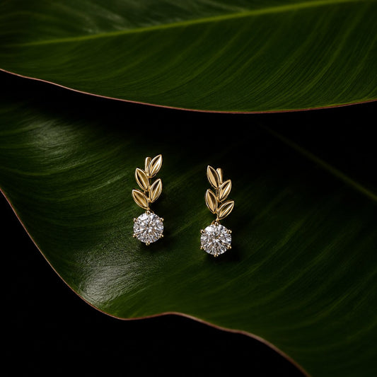 Botanical diamond earrings in gold with leaf-inspired design on tropical green leaf backdrop