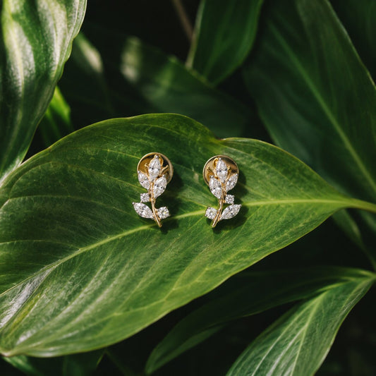 Gold floral diamond stud earrings with marquise-cut diamonds on lush green leaf background